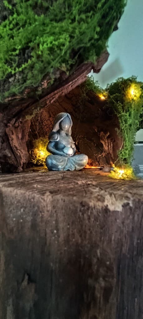 Megvilágított mini oltár: meditáló figura zuzmóval borított fatörzs-fülkében, apró meleg fényekkel