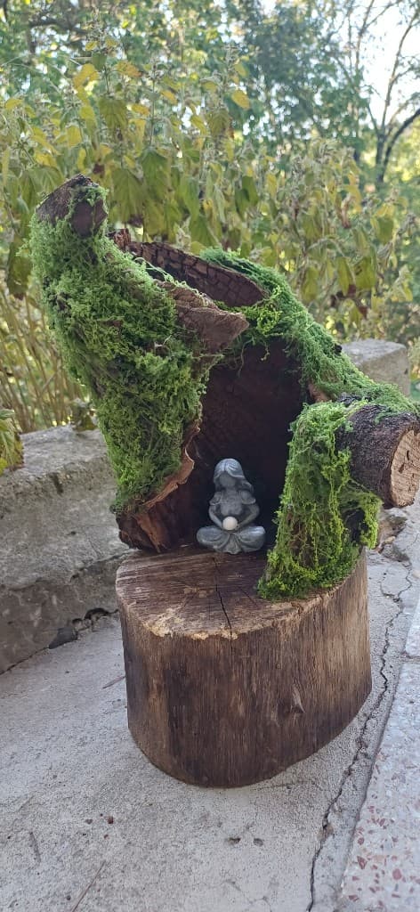 Kerti mini oltár tuskón: zuzmós fafülke és meditáló figura természetes fényben